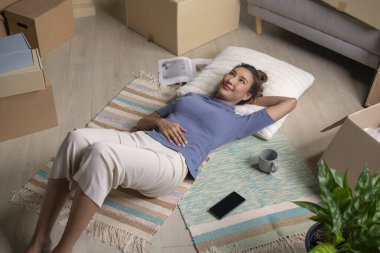 Yeni evde dinlenen mutlu Asyalı genç bir kadın. Taşındıktan sonra gülümseyen yüzüyle yerde yatıyor..