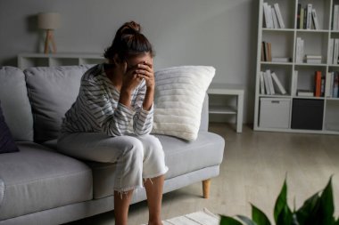 Genç Asyalı kadın evdeki koltukta oturup üzgün, yorgun ve endişeli zihinsel sağlıkta depresyon geçiriyor..