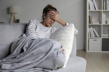 Zor durumdaki yalnız Asyalı kadın, endişeli, kafası karışık, evdeki kanepede uzanıyor. Kadın zihinsel sağlık sorunları yaşıyor.