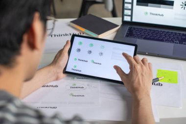 Bir ofis stüdyosunda çalışan, tablet kullanan, logo tasarlayan ve kurumsal kimlik ve logo tasarım sürecini gösteren Asyalı bir erkek grafik tasarımcısı..