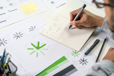 Logo tasarımları, logo tasarımları, logolar ve kurumsal kimlik ve logo tasarım sürecini gösteren notlar alan bir grafik tasarımcının yakın plan görüntüsü..
