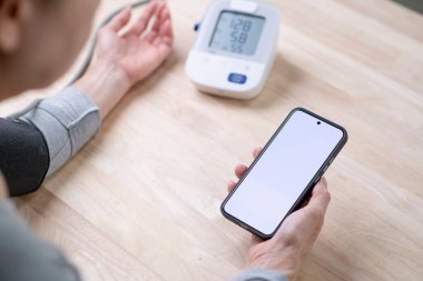 Telefondaki boş beyaz ekranla telefonda kan basıncı testi yaptıran bir kadın..