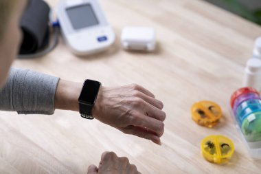 Orta yaşlı Asyalı kadın, kopyalama alanı için boş ekranı olan akıllı saatlerin ilaç hatırlatıcılarını kontrol ediyor ve.