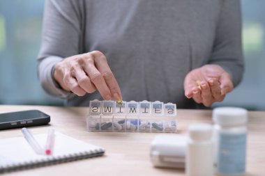 Orta yaşlı bir kadın günlük ilaç kutusundan alınan hapları elinde tutuyor..