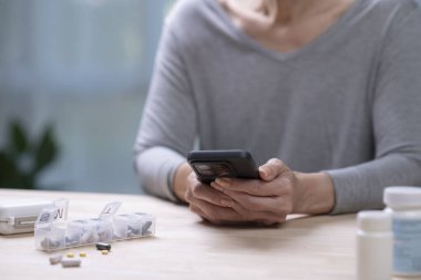 Orta yaşlı bir kadın telefonda ilaç hatırlatıcılarını kontrol ediyor..