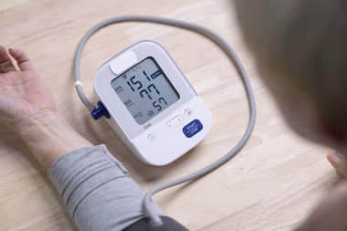 Orta yaşlı bir kadın tansiyon monitörünü ve kalp atış hızı monitörünü dijital basınç göstergesiyle kontrol ediyor. Sağlık ve Tıp Konsepti