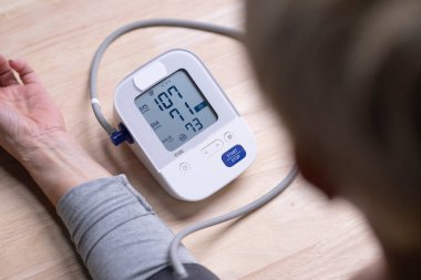 Orta yaşlı bir kadın tansiyon monitörünü ve kalp atış hızı monitörünü dijital basınç göstergesiyle kontrol ediyor. Sağlık ve Tıp Konsepti