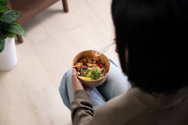 Asyalı bir kadın iş yerinde yemek yiyor, iş kadını ev ofisinde öğle yemeği molası veriyor.