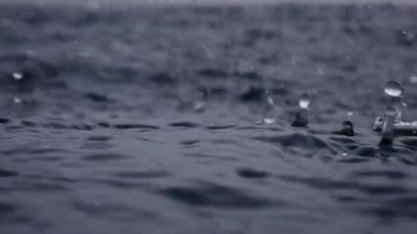 Sonsuz okyanusa yağmur damlaları düşer, yakın mesafeden. Kısa bir süre sonra deniz yüzeyine çarpar, ağır çekimde..