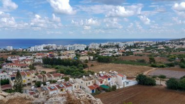 Top aerial view overlooking Protaras town with traditional houses with solar water heaters on roofs, fields nearby, and the Mediterranean sea on the horizon in Cyprus.