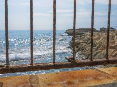 Kıbrıs Rum Kesimi 'nin başkenti Aye Napa' da güneşli bir günde Akdeniz ve kayaların üzerindeki paslı bir kilitle paslı köprü çitinden iskeleye doğru manzara.