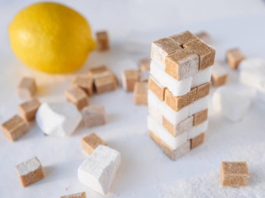 Beyaz ve kahverengi şeker küplerinden bir kule ve arka planda taze limon. Tatlı ve ekşi yemek konsepti.