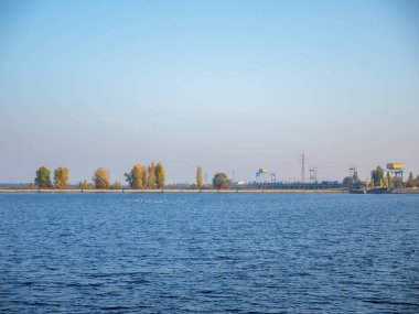 Büyük bir kuş sürüsü Kyiv deniz salyası üzerinde uçuyor, sakin mavi su yatı ve yüzen teknesi, mavi ve pembe gökyüzü, ufukta dar bir banka şeridi.
