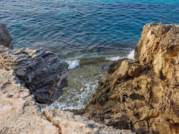 View from above over beautiful turquoise waves of blue Mediterranean sea coming on rough yellow and orange porous rocks  in Ayia Napa, Cyprus.