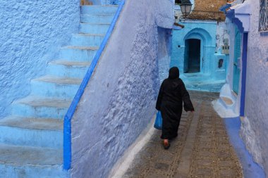 North Africa. Morocco. Chefchaouen. A maghrebin woman dressed in djellaba walking in a blue street of the medina