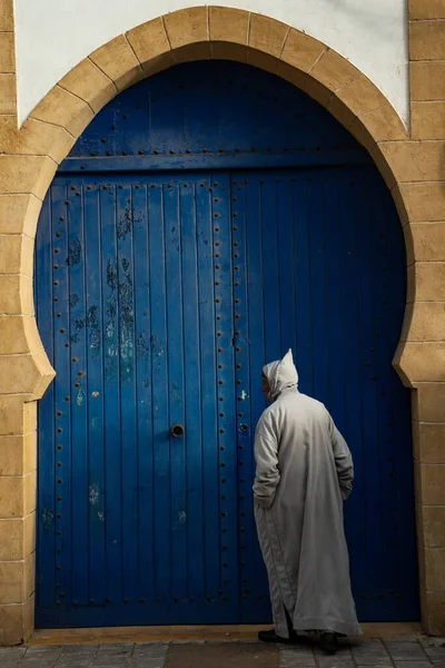 Fas 'ta. Essaouira. Caminin mavi kapısının önünde djellaba giymiş bir adam.