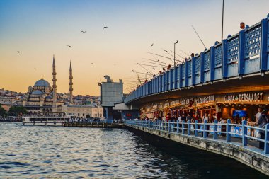 Hindi. İstanbul. İstanbul 'daki Galata Köprüsü üzerinde gün batımında, demiryolu ve görkemli Yeni Cami boyunca dizilmiş balıkçılar (Yeni Cami))