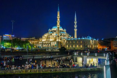 Hindi. İstanbul. Görkemli Yeni Cami 'nin gece manzarası. Güzelce aydınlatılmış. Boğaz boyunca yürüyen ve dinlenen insanlar.