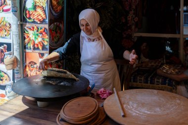 Hindi. İstanbul. Balat bölgesi. Bir sokak yemeği standında geleneksel bir mutfakta bir kadın büyük yuvarlak bir ızgara üzerinde yassı ekmek hazırlar.