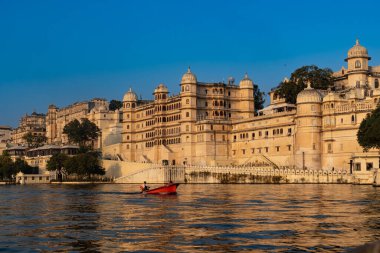 Hindistan. Rajasthan. Udaipur. Alacakaranlıkta şehir sarayının önündeki Pichola Gölü 'nde küçük bir tekne hareket eder.