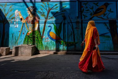 Hindistan. Rajasthan Eyaleti. Jodhpur. Kırmızı sarili Hintli bir kadın şehrin caddesinde bir duvar resminin önünden geçiyor.