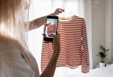 Akıllı telefondaki çizgili tişörtün fotoğrafını çeken kadın. 