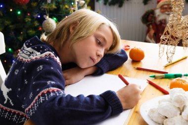 Özenli çocuk Noel Baba 'ya arka planda Noel ağacı ile mektup yazıyor.
