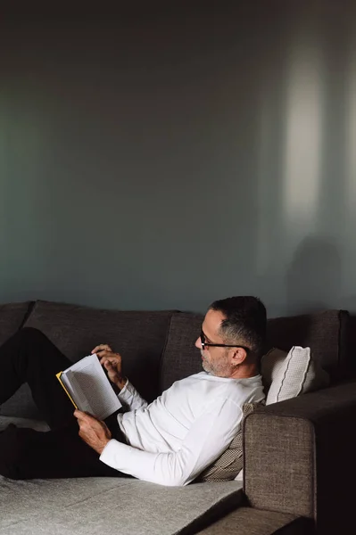 Midaldrende Mand Med Briller Læse Bog Derhjemme Sofaen - Stock-foto