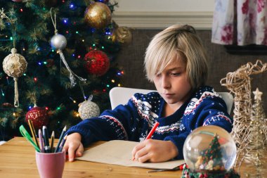 Özenli çocuk Noel Baba 'ya arka planda Noel ağacı ile mektup yazıyor.