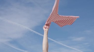 Woman hand spinning clothes in hand against blue sky, slow motion.