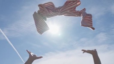 Throwing pre owned clothes against blue sky in slow motion, low angle view, sustainable fashion concept.