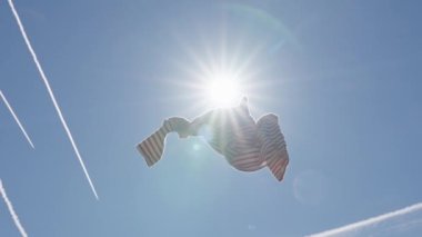 Throwing pre owned clothes against blue sky in slow motion, low angle view, sustainable fashion concept.