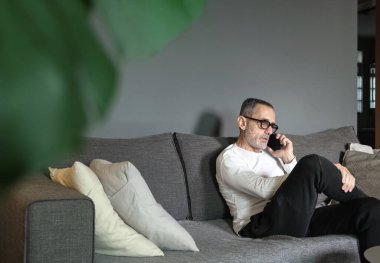 Gözlüklü orta yaşlı bir adam evde çalışırken telefonda konuşuyor..