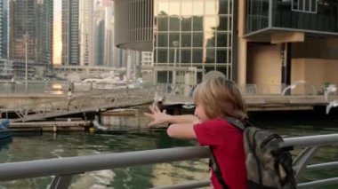 Cheerful cute boy laughing and feeding seagulls. Happy vacation in Dubai