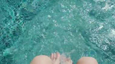 Girl dangles her legs in the water of the pool