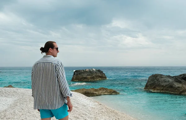 Młody Człowiek Stojący Plaży Błękitnym Morzem Skałami Humorzastym Niebem Tle — Zdjęcie stockowe