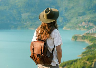 Şapkalı ve sırt çantalı gezgin Dağların ve gölün güzel manzarasının tadını çıkarıyor 