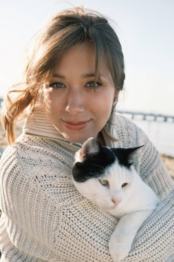 Neşeli genç bir kadının açık hava portresi. Kedisiyle mutlu bir anı paylaşıyor.