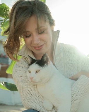 Neşeli genç bir kadının açık hava portresi. Kedisiyle mutlu bir anı paylaşıyor.