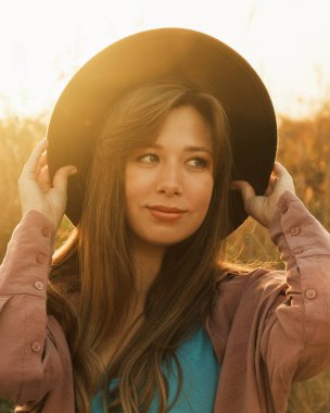 Kahverengi şapkalı, neşeli bir gülümsemesi olan genç bir kadın, altın saat ışığıyla yıkanmış..