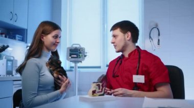 Veteriner yavru köpek sahibine evcil hayvan sağlığıyla nasıl ilgileneceğini açıklıyor. Modern bir veteriner kliniğinde Yorkshire Teriyeri 'ni kollarında tutan bir kadın. Yüksek kalite 4k görüntü