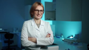 Gözlüklü bir veteriner kameraya kollarını kavuşturup gülümsüyor. Mavi ışıklı bir laboratuvarda. Ciddi görünüyor ama mutlu. Yüksek kalite 4k görüntü 