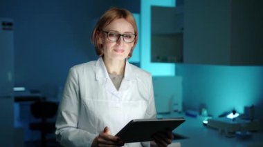 Beyaz önlüklü ve gözlüklü bir veteriner tablet bilgisayardan bakıp gülümsüyor. Laboratuvarda ve gözlük takıyor. Odaklanmış görünüyor. Yüksek kalite 4k görüntü 