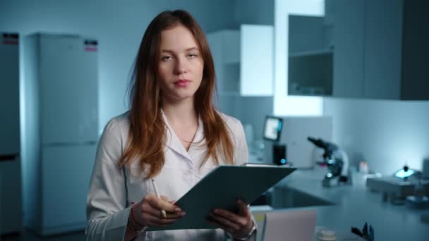 一位女医生在看相机前 在平板电脑上检查了一些东西 她在一个蓝光的实验室里 她看起来很严肃 但很快乐 高质量的4K镜头 — 图库视频影像
