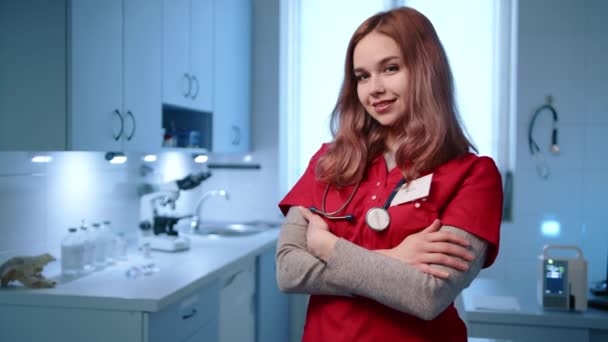 笑着可爱的年轻女兽医站在动物医院的一间轻便的现代化办公室里 医生穿着医生的西服 带着听诊器 双手交叉 高质量的4K镜头 — 图库视频影像
