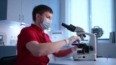 Genç ve yetkin bir erkek veteriner, laboratuvar araştırmalarına dürbün mikroskobu kullanarak odaklanır. Doktor mikroskop kurup araştırma yapıyor. Yüksek kalite 4k görüntü