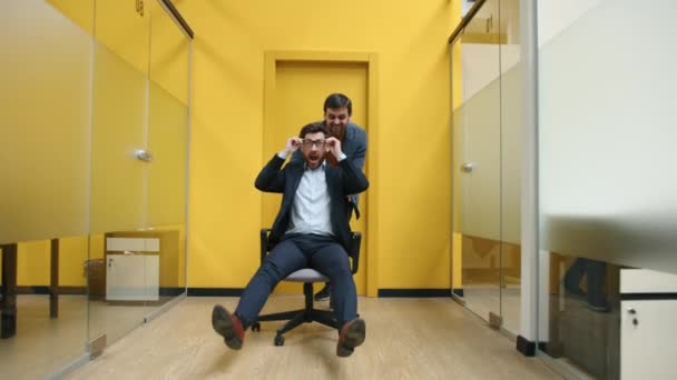 明るく屈託のない男たちが幸せそうな姿をクローズアップ 近代的な空間の廊下だけでオフィスチェアに乗る成功した同僚 高品質4K映像 — ストック動画