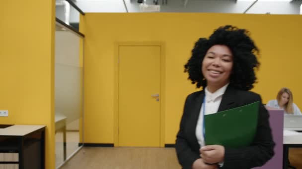 廊下に沿って室内を歩く陽気で笑顔の女性の専門家の閉鎖 成功したアフリカ系アメリカ人女性の肖像画は 重要な文書とフォルダを保持 高品質4K映像 — ストック動画