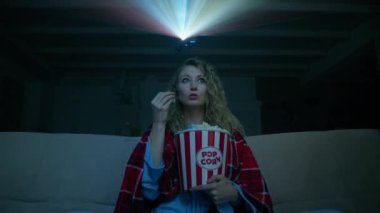 Battaniyeye sarılı genç bir kadın patlamış mısırlı bir filme katılıyor. Ev sinemasında aksiyon filmi izleyen heyecanlı bir kadın. Yüksek kalite 4k görüntü