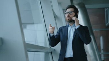 Gözlük takan stresli bir girişimcinin yakın çekimi. Resmi takım elbiseli sinirli adamın portresi modern ofiste duygusal bir telefon görüşmesi yapıyor. Yüksek kalite 4k görüntü